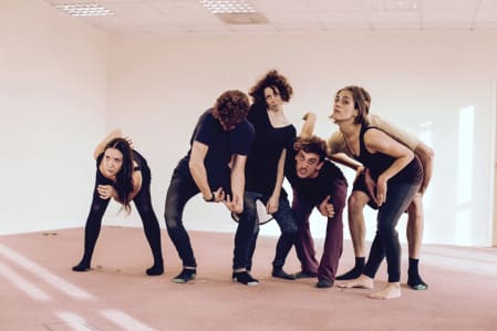 A photo of six performers posing in varied positions in a white studio space