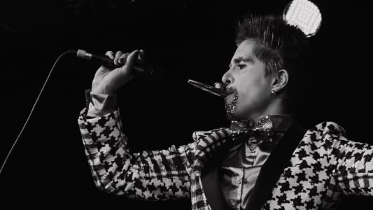 A black and white close up of drag king Tito Bone singing into a mic