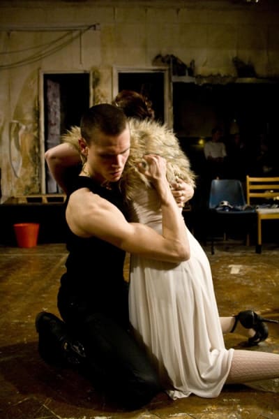 A photo of two people in costume kneeling on the floor in a dramatic pose, in a dark indoor space