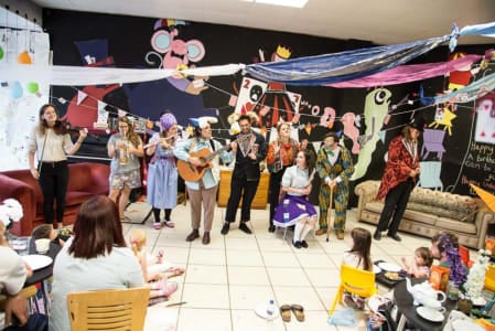 A photo of performers dressed in colourful clothes performing to adults and children with musical instruments