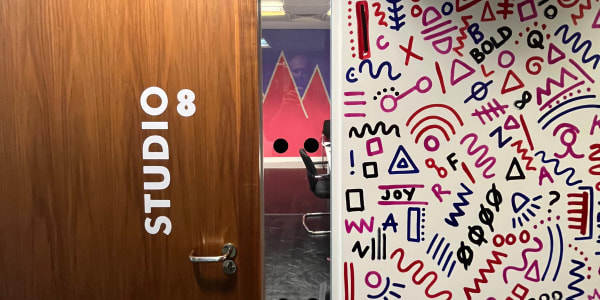 Door to Studio 8 in London with a window showing a mural inside the studio and the adjoining wall with a mural of abstract patterns and words.