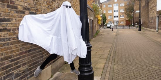 Link to Your Progress Will be Saved. A person dressed as a ghost in a white sheet with sunglasses dances around a lamppost