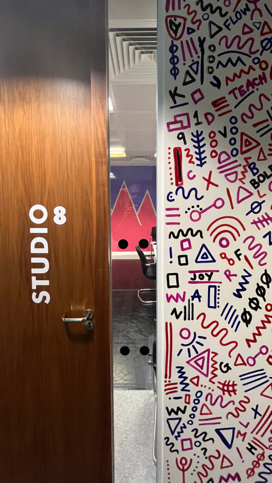 Door to Studio 8 at Theatre Deli. Through window you can see purple triangle designs in studio. To right of window you can see complimentary abstract patterns including words such as 'joy'