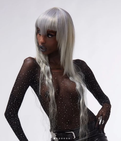 Woman against a white background, she is wearing a long grey wig
