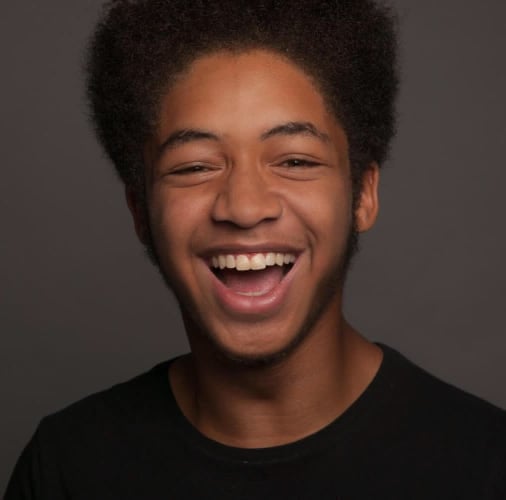 A photo of CJ, a young black man. He is has a big smile and is wearing a black t shirt