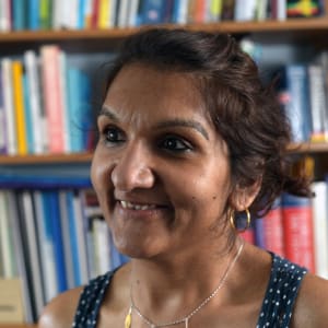 Headshot of Sonali, a British Indian woman, smiling in front of a bookcase.