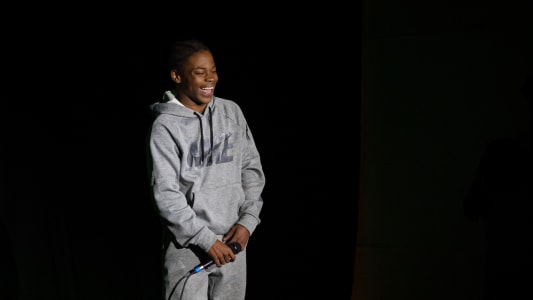 Tiger stands onstage laughing and wearing a grey track suit