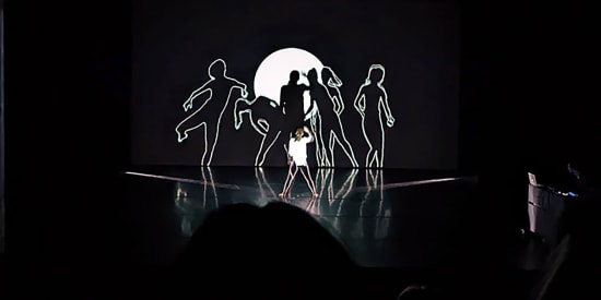 Link to Retraced page. A person dances on stage in front of projected sillouhettes of dancers.