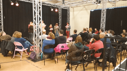 A photo of an audience watching a reading by six performers holding scripts on the Eyre Street Theatre Deli stage