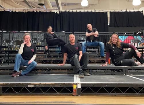 A photo of the Theatre Deli Sheffield team in 2019, sitting on a seating rake and smiling