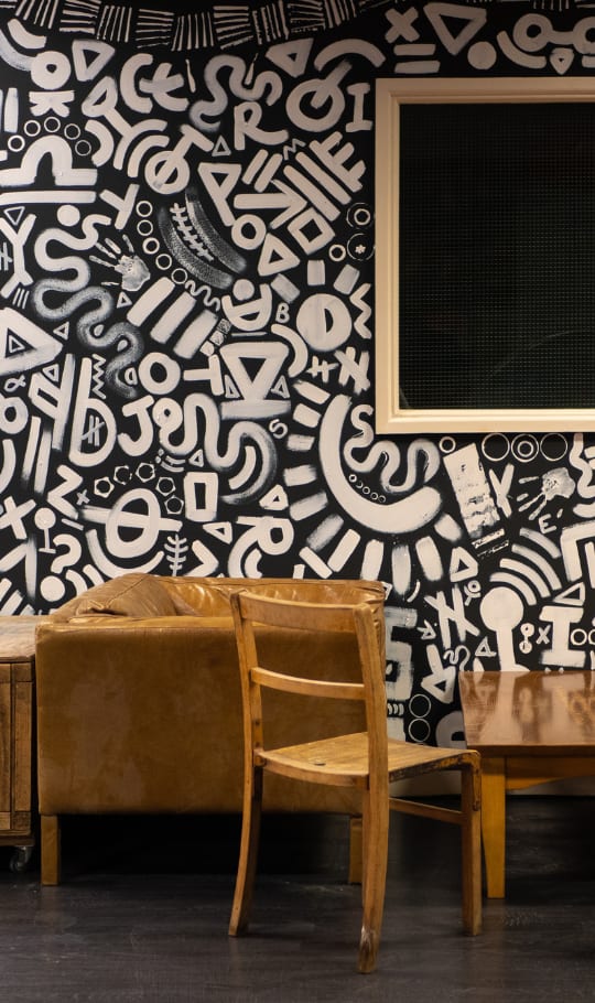 Abstract white design on black wall with brown tables and chairs in the foreground