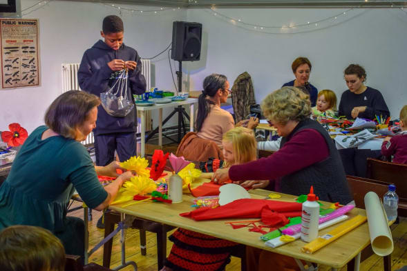 A photo of young people and adults making crafts at tables and chairs in a room