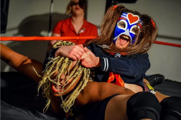 A photo of two people wrestling in a wrestling ring, one of them is wearing a blue and red mask