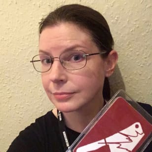 Selfie of Jen, a white woman with brown hair wearing glasses and holding up her Theatre Deli lanyard.